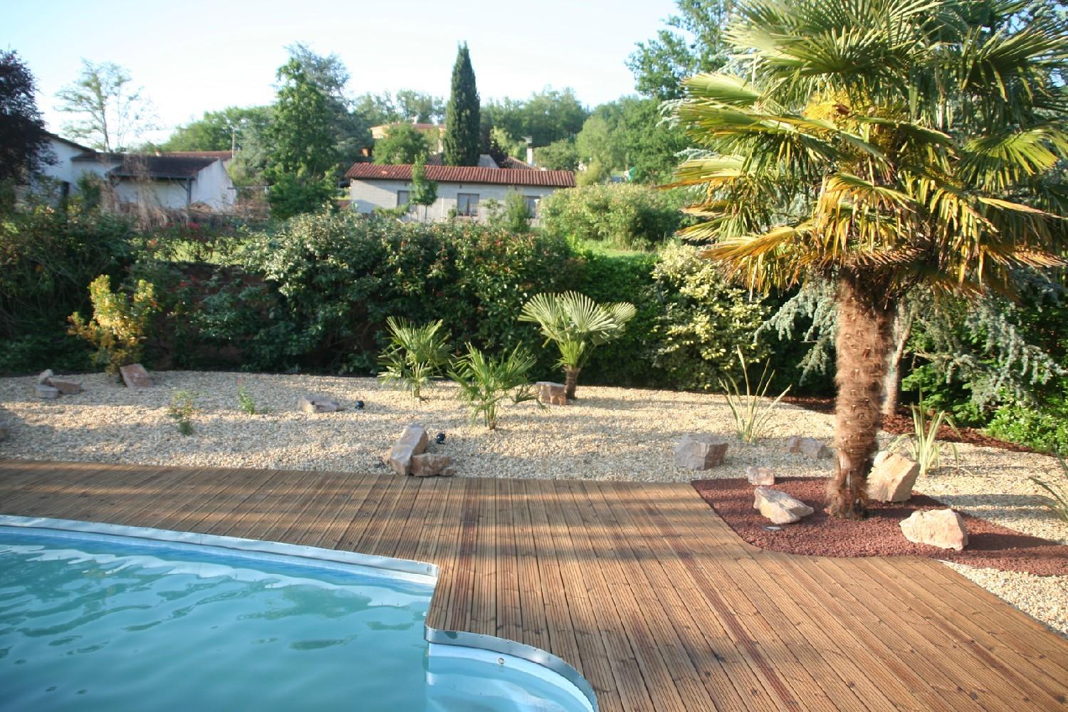 Terrasse bois en pin en abords de piscine avec rive courbe en inox. Massif d'agrément surfacé gravier